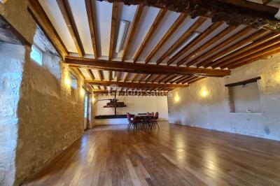 Pressoir ancien en bois dans une pièce avec murs en pierre, plafond à poutres apparentes et sol en parquet.