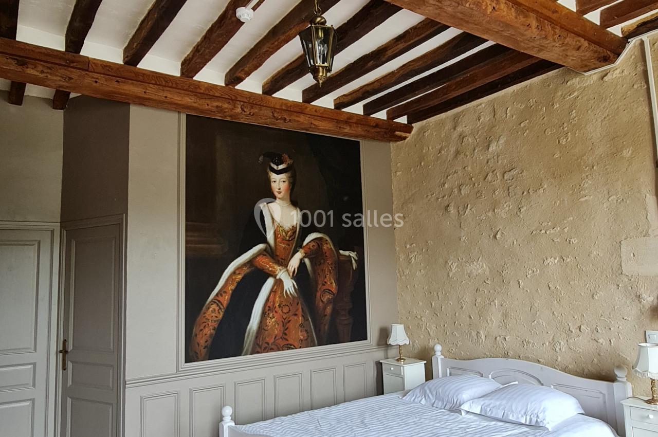 Chambre avec lit double, poutres apparentes, mur en pierre et grand tableau représentant une femme en tenue d'époque.