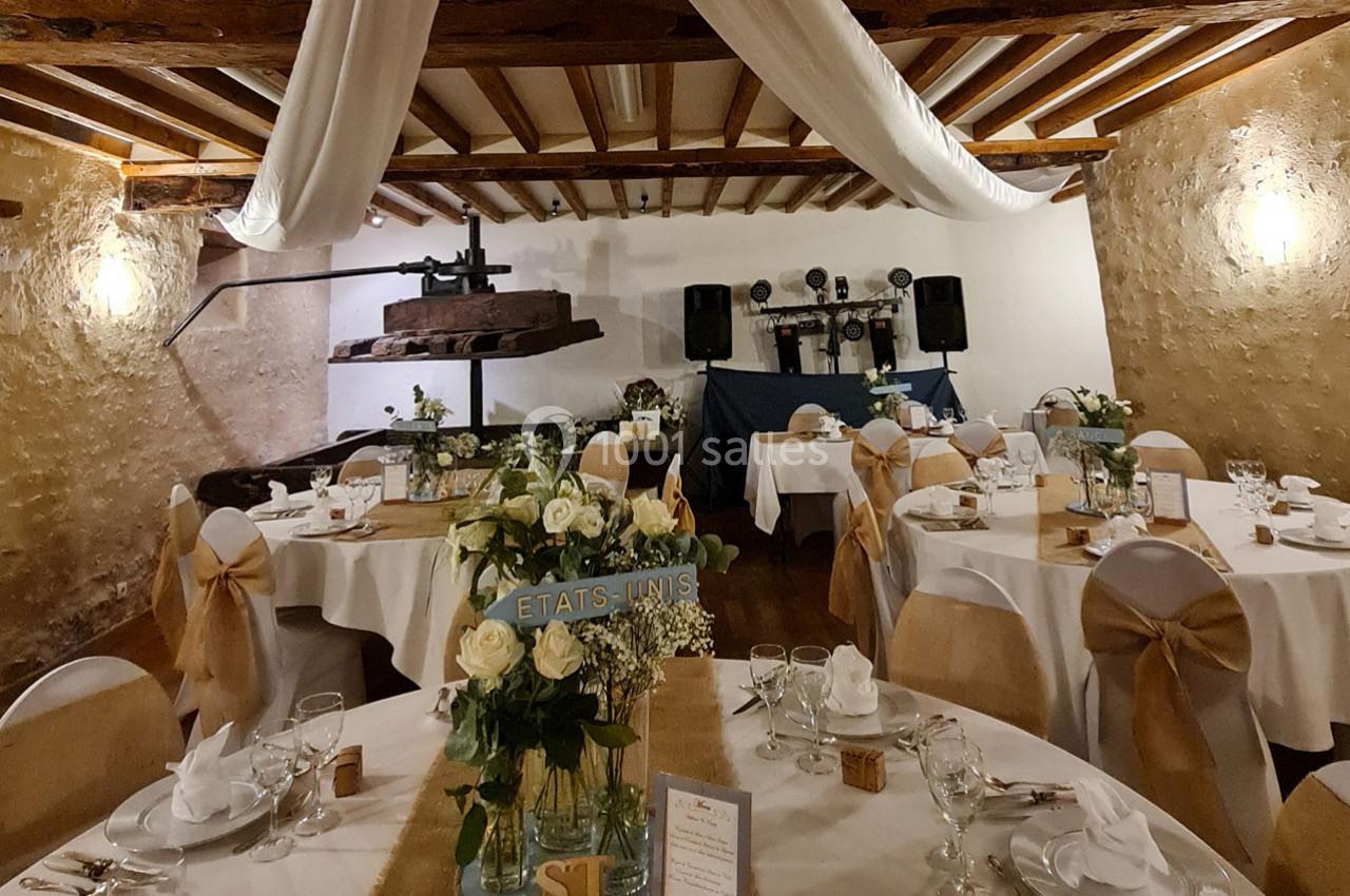 Salle de réception décorée pour un mariage, avec tables dressées, fleurs blanches et éléments rustiques en bois.
