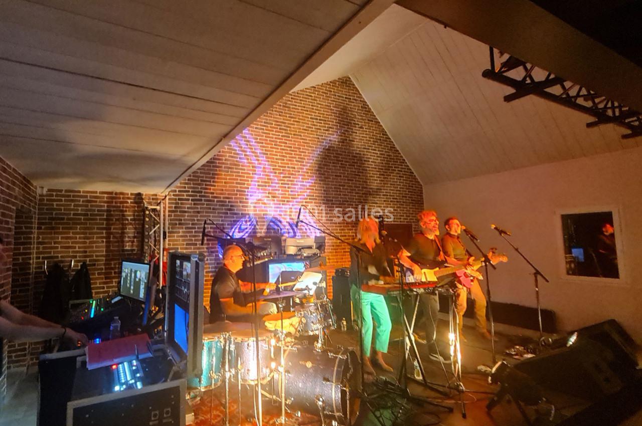 Un groupe de musiciens joue sur scène dans une salle en briques, éclairée par des lumières colorées.