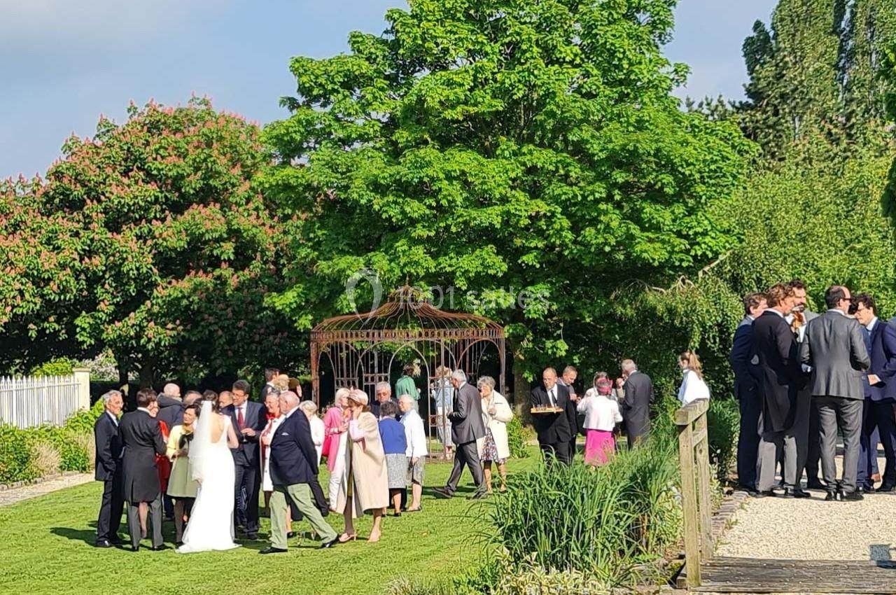 Groupe de personnes rassemblées dans un jardin lors d'une réception, avec une mariée en robe blanche au premier plan.