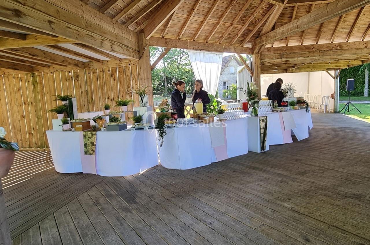 Deux personnes préparent un buffet décoré sous une structure en bois ouverte, entourée de verdure.