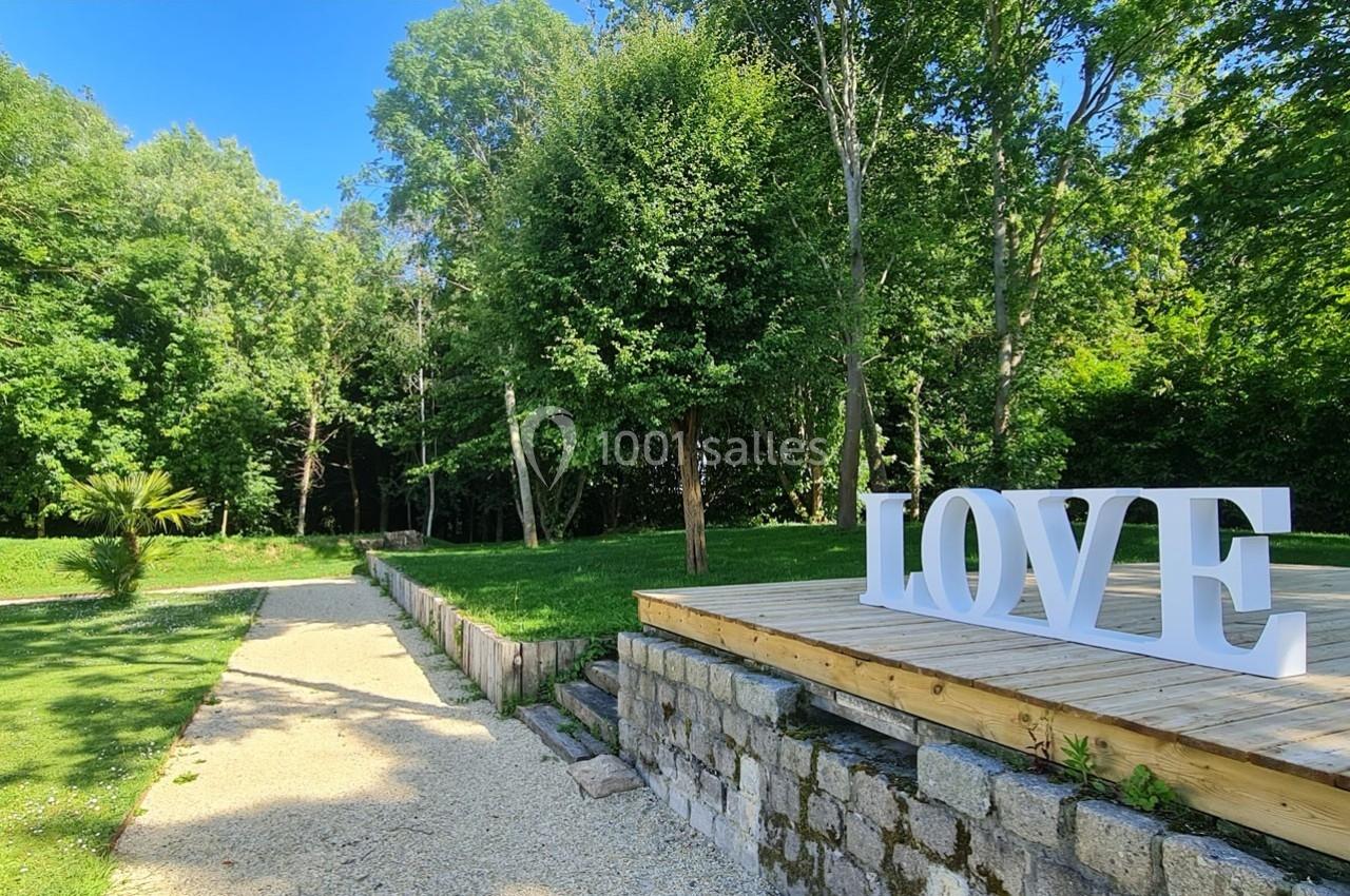 Chemin en gravier bordé de verdure menant à une plateforme en bois avec le mot ’LOVE’ en lettres blanches.