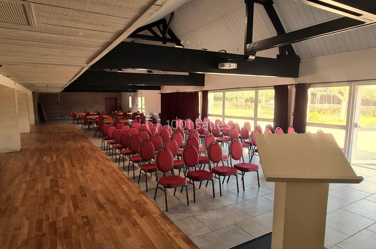Salle de conférence lumineuse avec rangées de chaises rouges alignées face à un pupitre en bois clair.