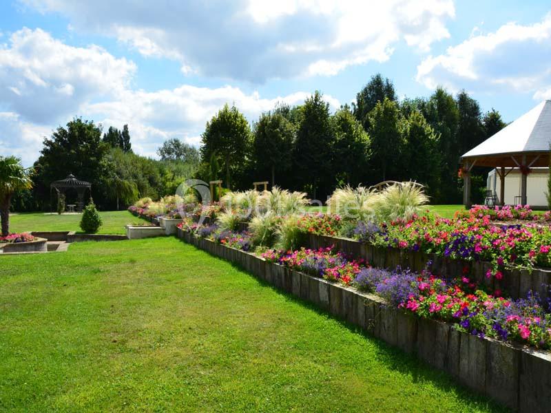 Jardin paysager avec pelouse, massifs de fleurs colorées en terrasses et structures en bois sous un ciel partiellement…