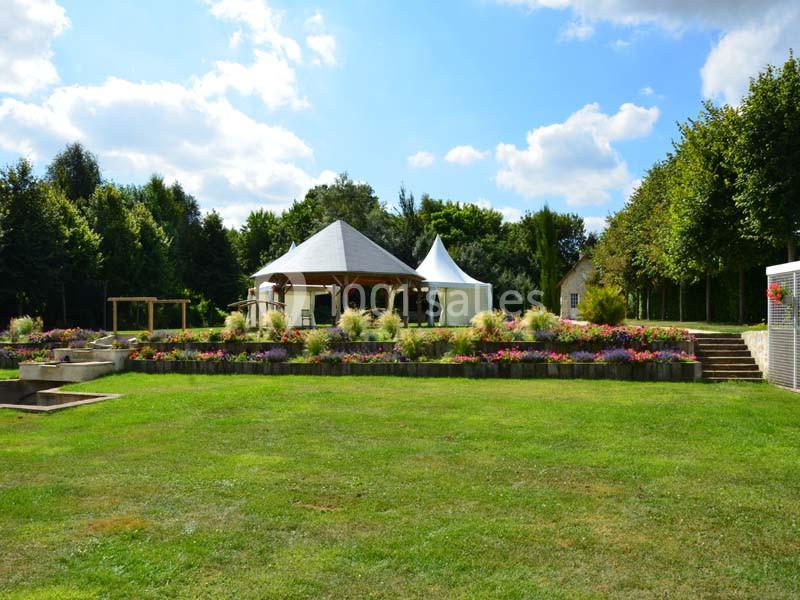 Un jardin verdoyant avec pelouse, parterres de fleurs colorées et une structure en bois avec toit et tente blanche.