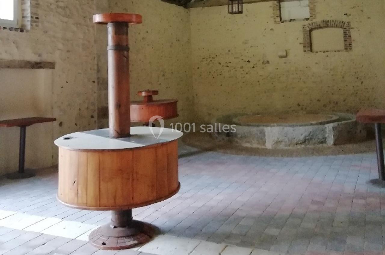 Salle ancienne avec un sol en pavés, contenant un fourneau en bois et métal au premier plan et une cuve en pierre au fond.