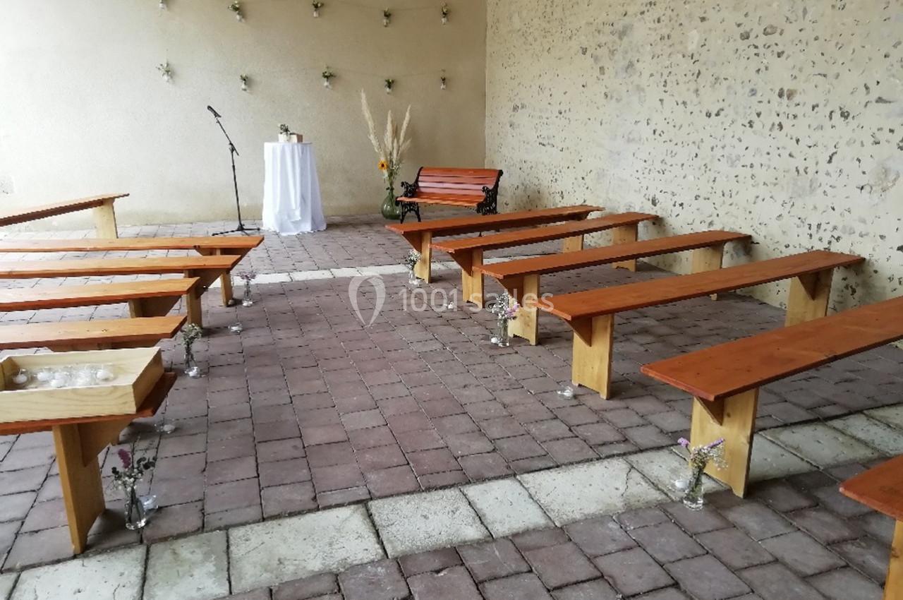 Bancs en bois disposés dans une cour pavée avec un pupitre, une table décorée et des fleurs en arrière-plan.