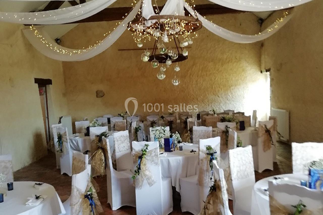 Salle de réception décorée avec des chaises blanches ornées de rubans, des guirlandes lumineuses et des drapés suspendus.