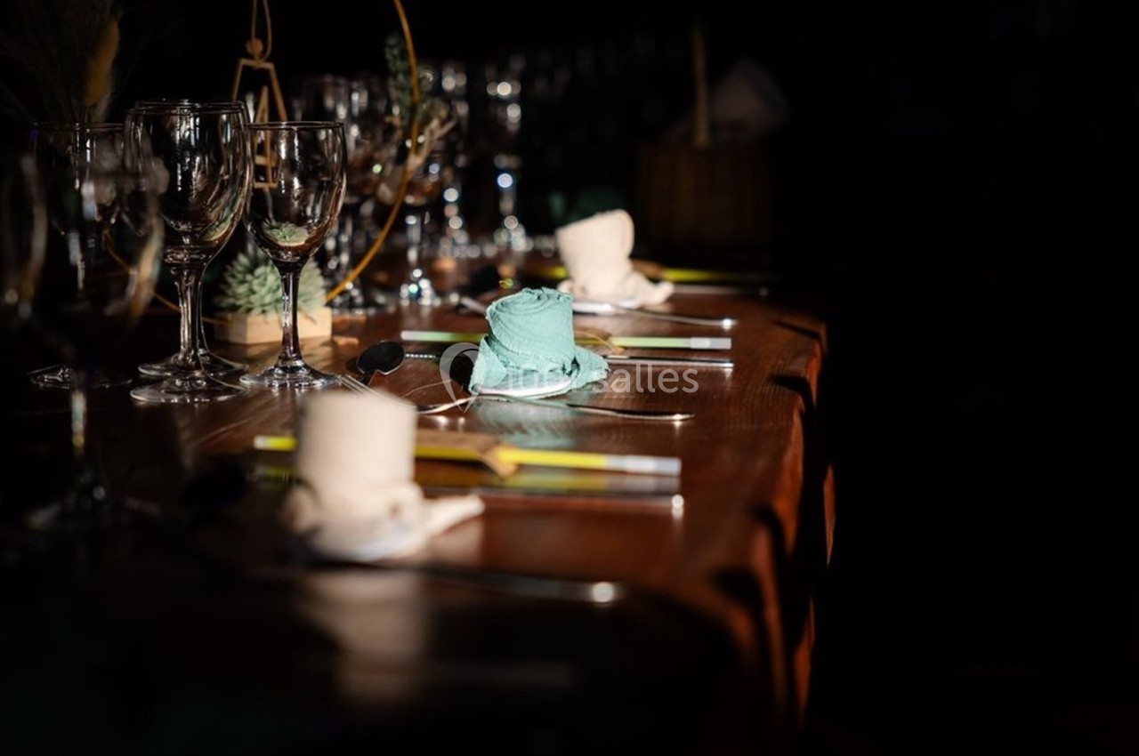 Table dressée avec des serviettes roulées, verres à pied et couverts, éclairée par une lumière tamisée.