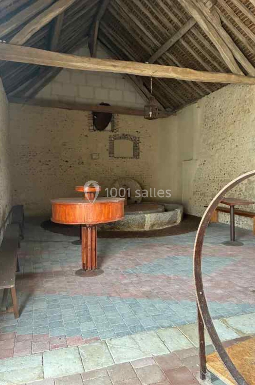 Intérieur d'une ancienne salle avec murs en pierre, toit en bois, bancs, et une cuve en pierre au centre.