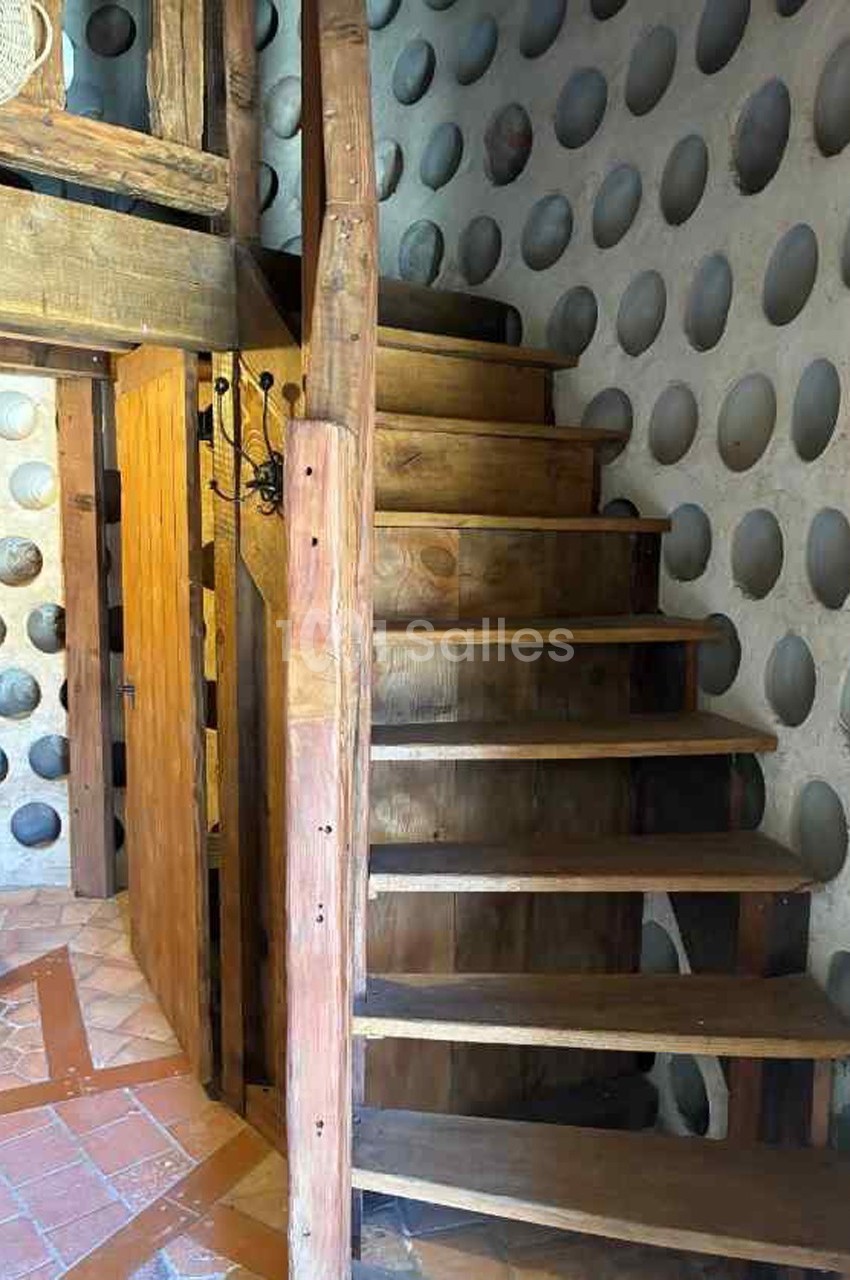 Escalier en bois avec rampe, dans une pièce aux murs ornés de motifs circulaires et sol en carreaux de terre cuite.