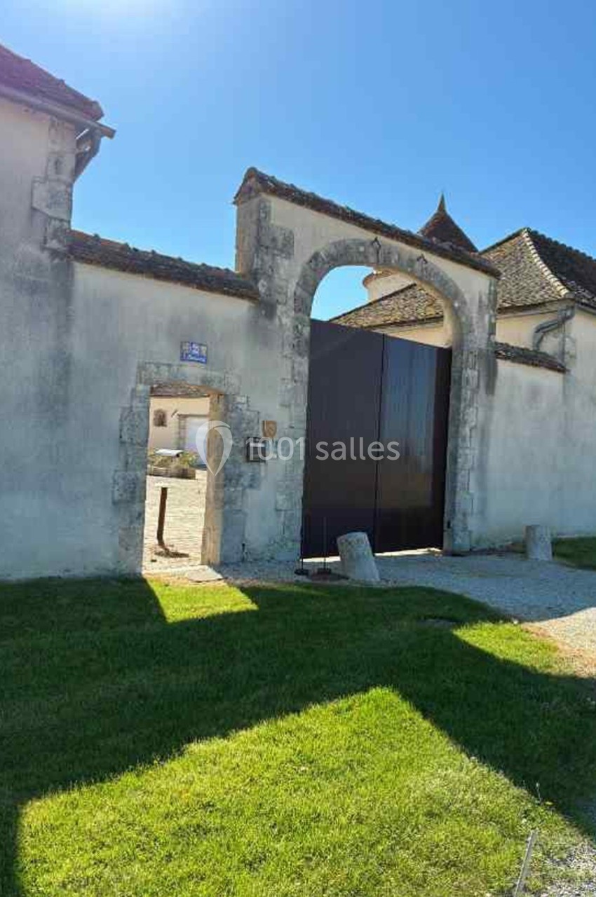Portail en bois sombre et petite porte piétonne dans un mur en pierre, entourés d'herbe et éclairés par le soleil.