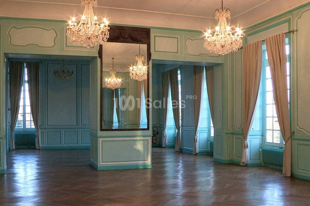 Salle élégante avec parquet en bois, murs bleu clair, miroirs, lustres en cristal et grandes fenêtres avec rideaux beiges.
