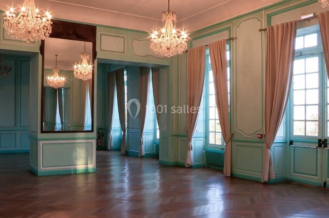 Salle lumineuse avec parquet en bois, murs turquoise, grands miroirs, lustres et rideaux beiges encadrant des fenêtres.