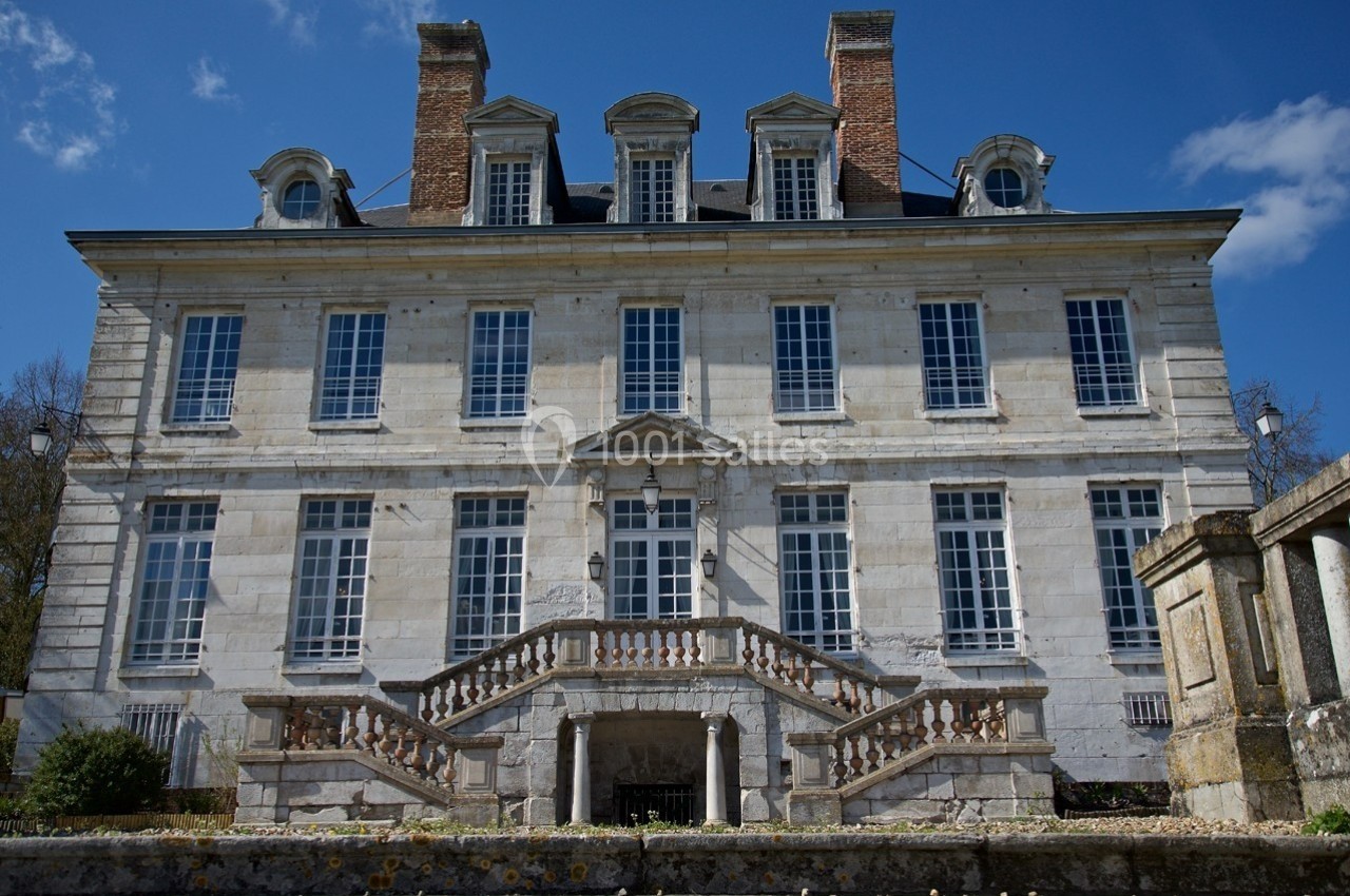 Façade d'un manoir en pierre avec plusieurs fenêtres à petits carreaux et un escalier symétrique à balustrade.