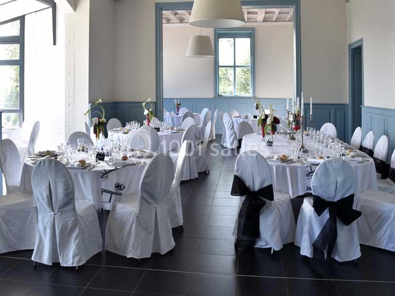 Salle de réception élégamment décorée avec des tables rondes dressées, nappes blanches et chaises ornées de nœuds noirs.