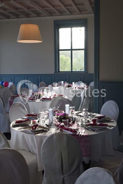 Salle de réception avec tables rondes dressées, nappes blanches, vaisselle élégante et lumière naturelle provenant d'une…