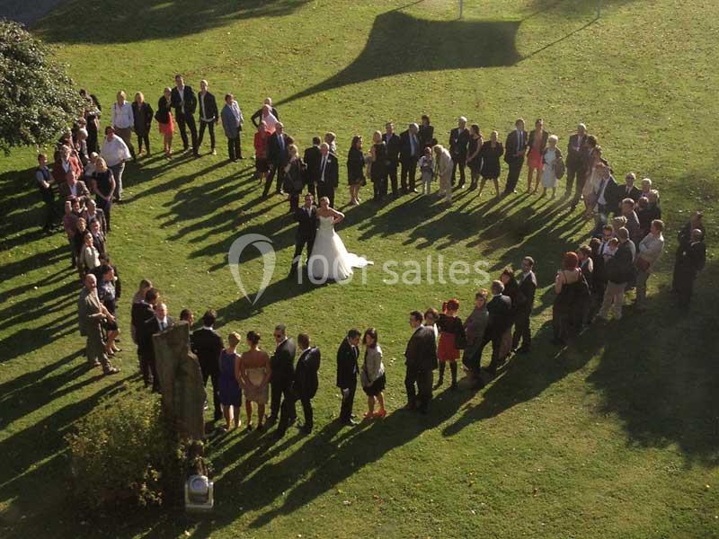 Des invités forment un grand cercle autour d'un couple de mariés sur une pelouse ensoleillée.