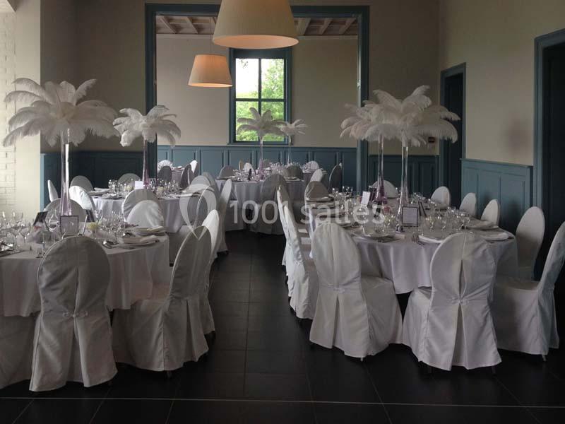 Salle de réception décorée avec des tables rondes, nappes blanches, housses de chaises et centres de table à plumes blanches.