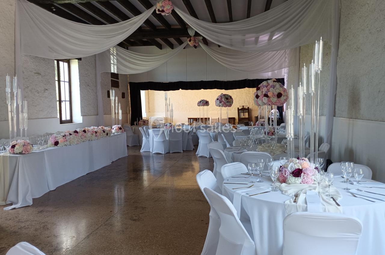 Salle de réception décorée avec des nappes blanches, des compositions florales et des chandeliers élégants.