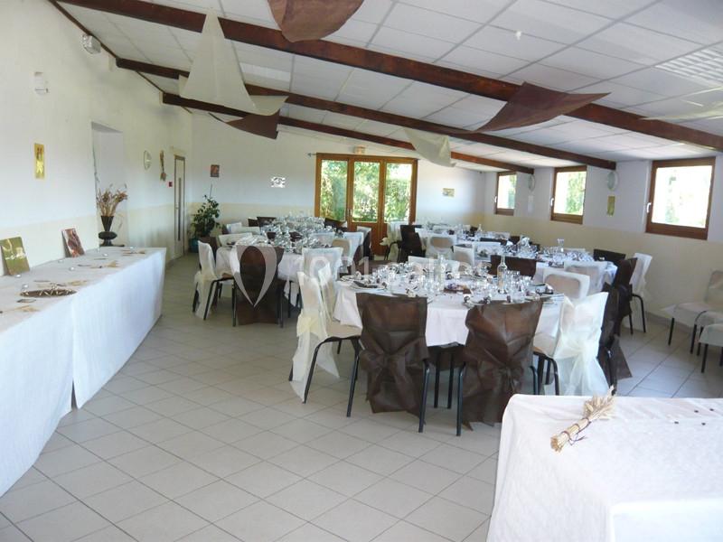 Salle de réception lumineuse avec tables dressées pour un événement, décorée de nappes blanches et chaises ornées.