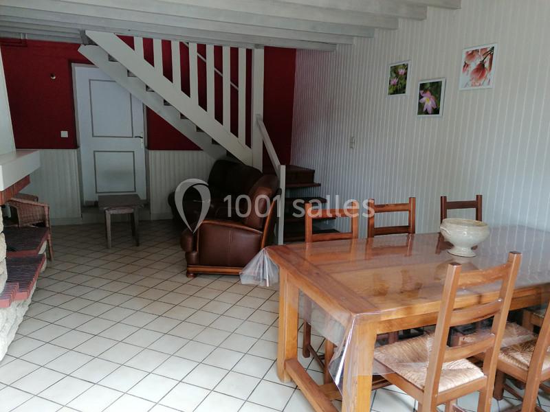Salle de séjour avec table en bois, chaises, canapé en cuir, escalier blanc et murs décorés de cadres floraux.