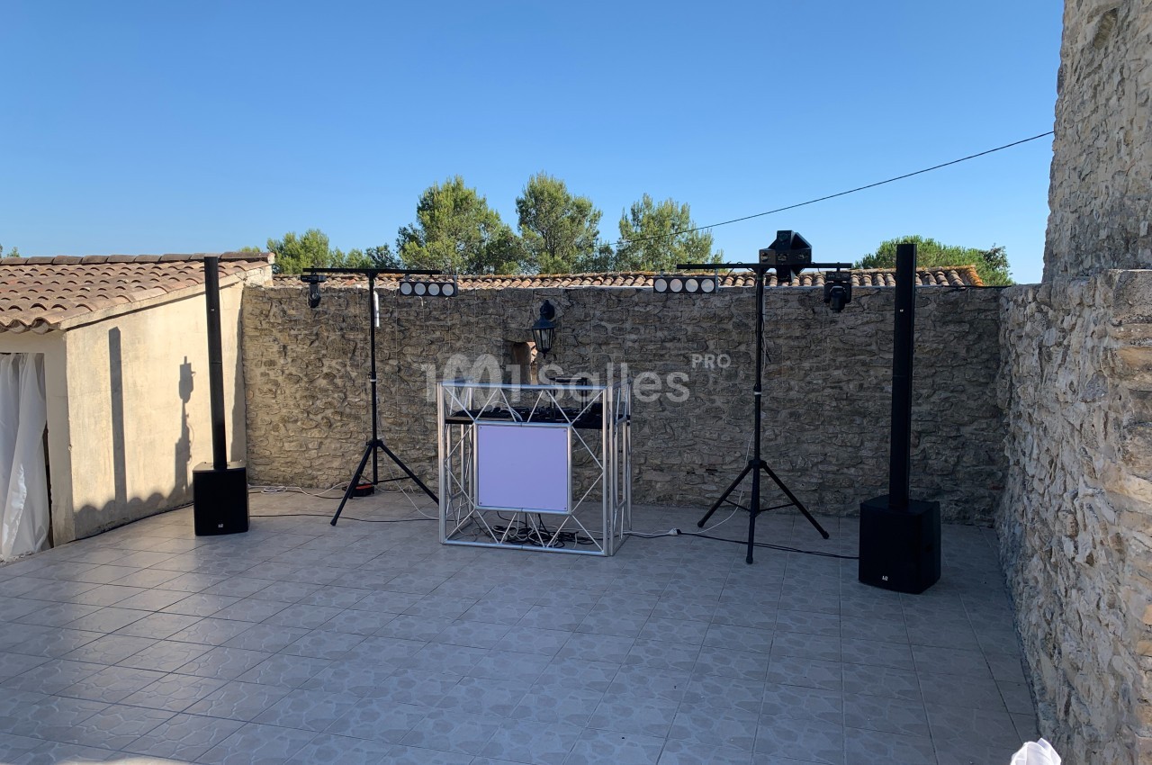 Installation de matériel de sonorisation et d'éclairage en extérieur, sur une terrasse en pierre entourée de murs en pierre.