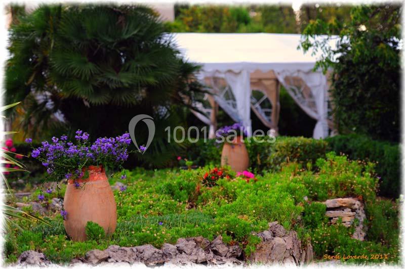 Location salle La Cadière-d'Azur (Var) - Château de Rochebelle - Var #4 Jardin fleuri avec des jarres en terre cuite, des plantes colorées et une tente blanche en arrière-plan.