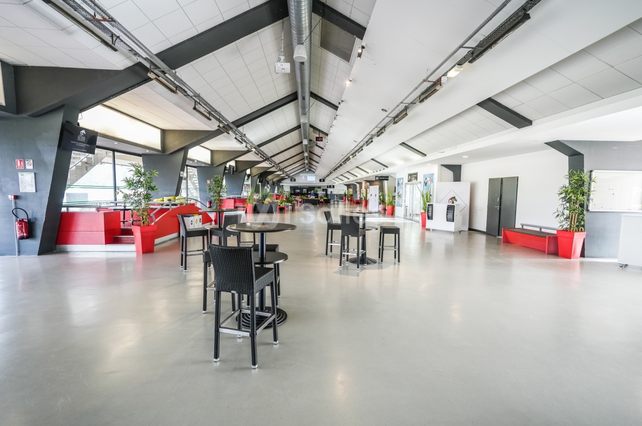 Vue d'un espace intérieur spacieux avec des tables, des chaises, des plantes et des zones d'assise rouges.