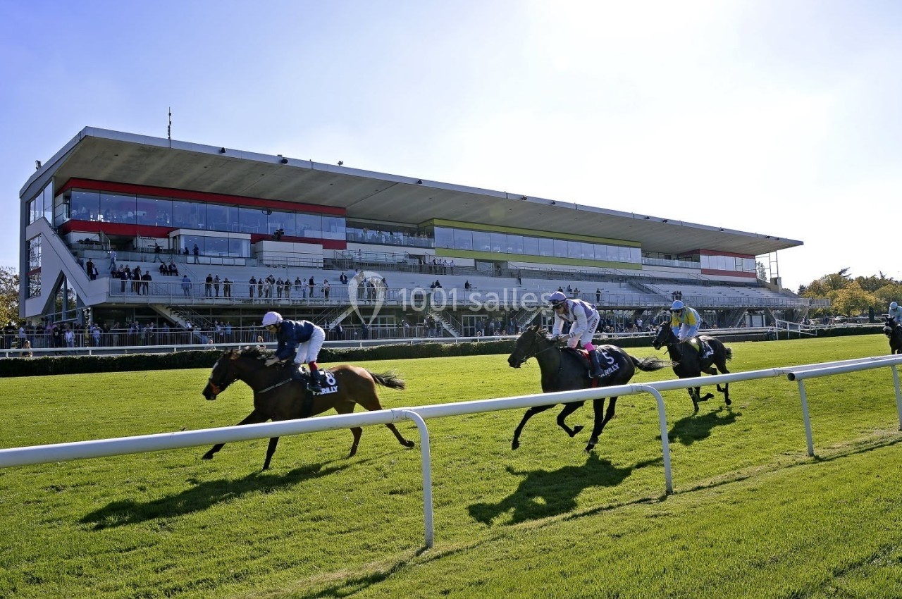 Des chevaux montés par des jockeys courent sur une piste d'hippodrome devant des tribunes remplies de spectateurs.
