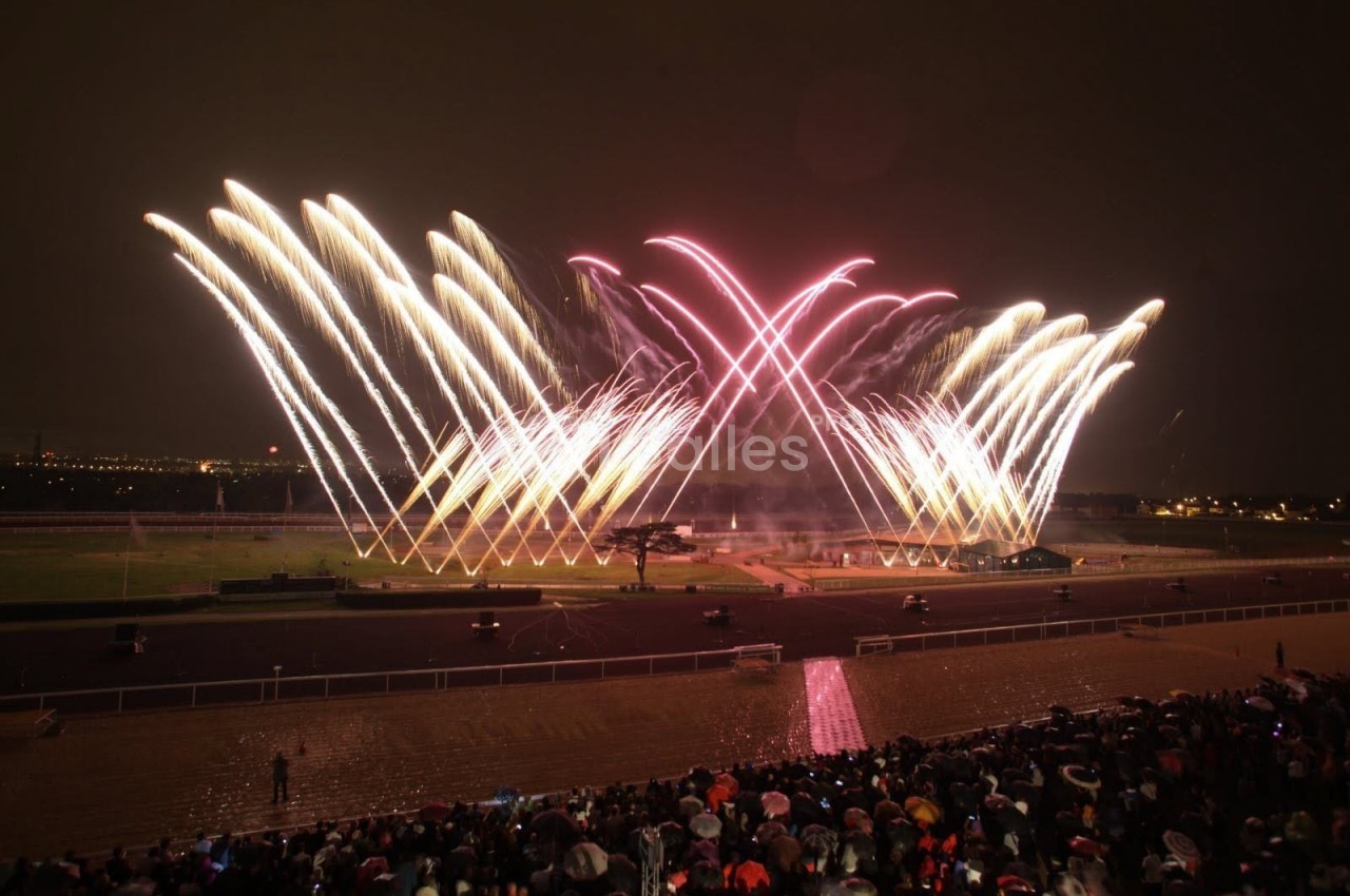 Feu d'artifice illuminant le ciel nocturne avec des spectateurs rassemblés sous un ciel sombre.