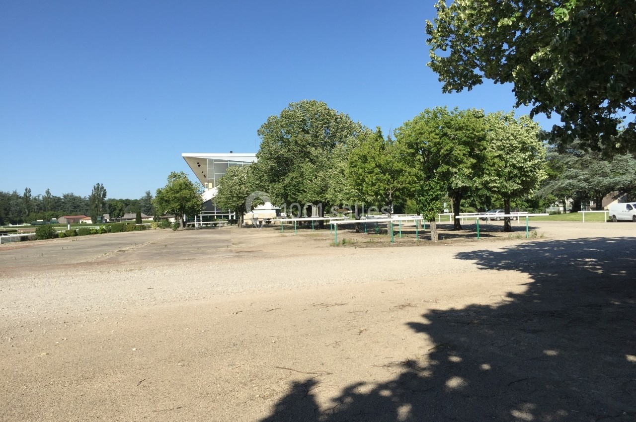 Vue d'un espace extérieur avec des arbres, une structure blanche en arrière-plan et un sol partiellement ombragé.