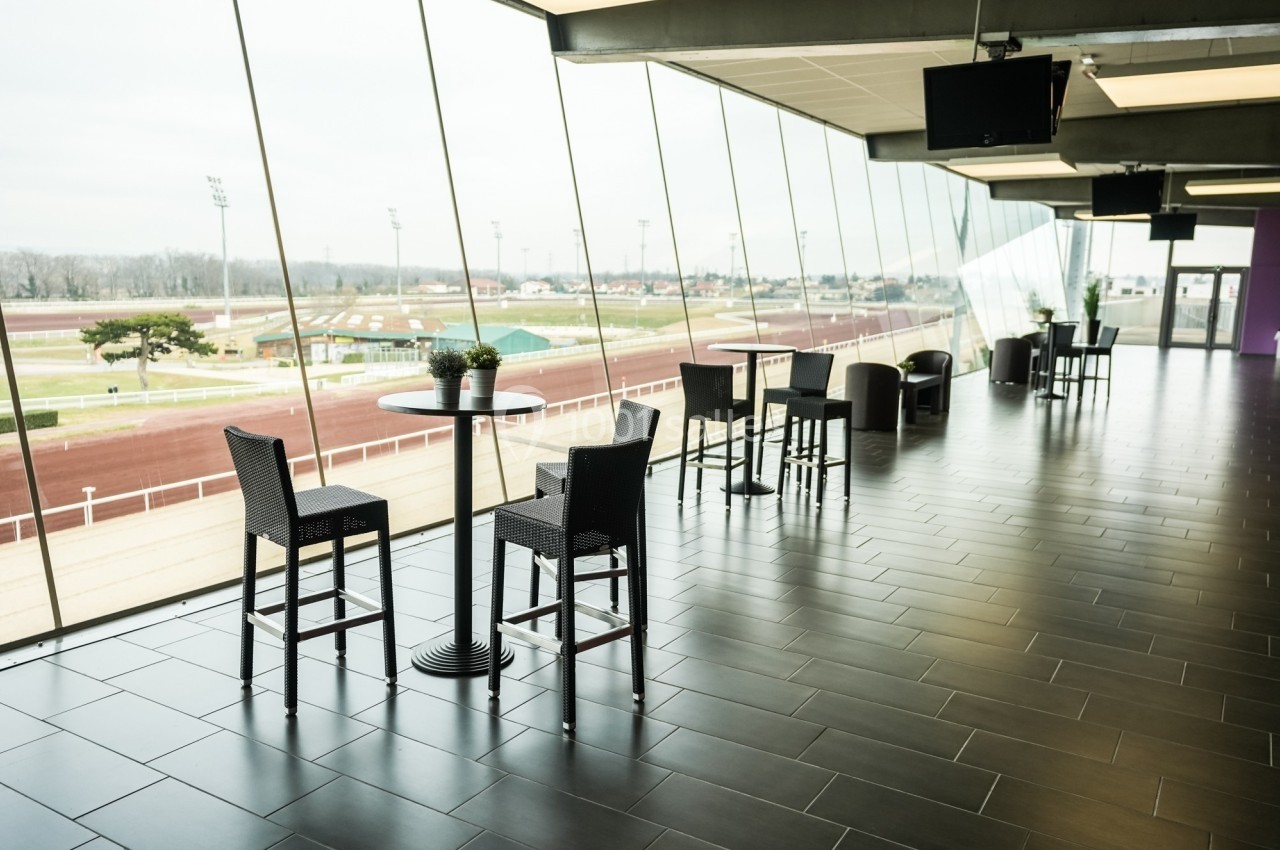 Salle avec de grandes baies vitrées donnant sur une piste extérieure, aménagée avec tables et chaises hautes.