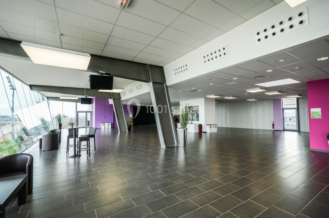 Salle spacieuse avec sol en carrelage sombre, murs blancs et roses, grandes fenêtres et mobilier minimaliste.