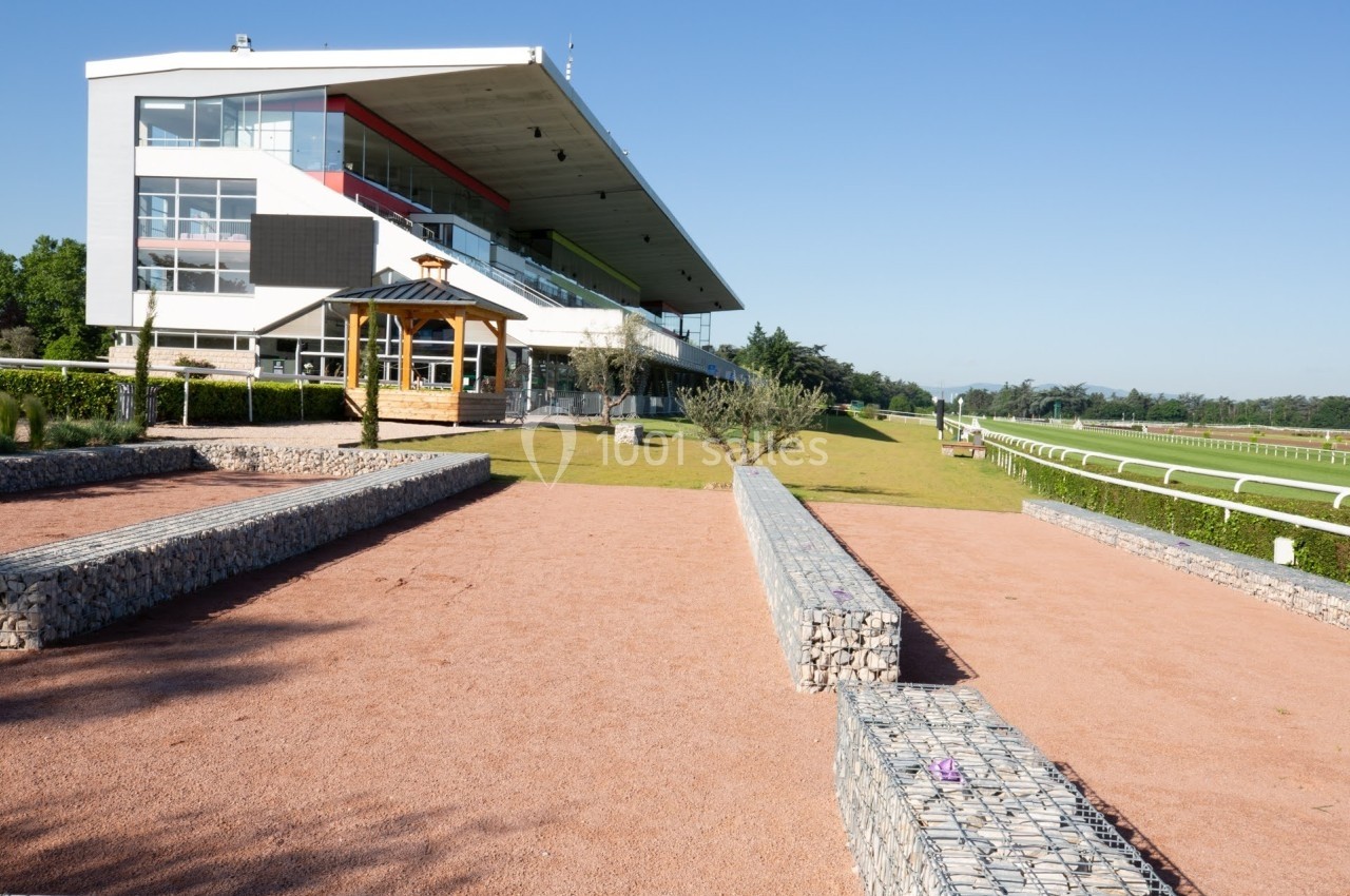Vue d'une tribune moderne près d'une piste de course, entourée d'espaces verts et d'aménagements en pierre.