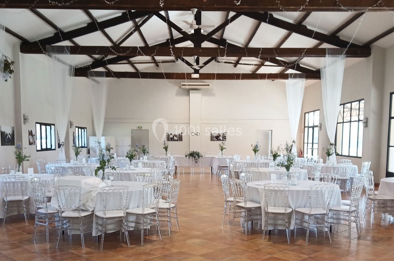 Salle de réception lumineuse avec tables rondes décorées de nappes blanches et chaises transparentes.
