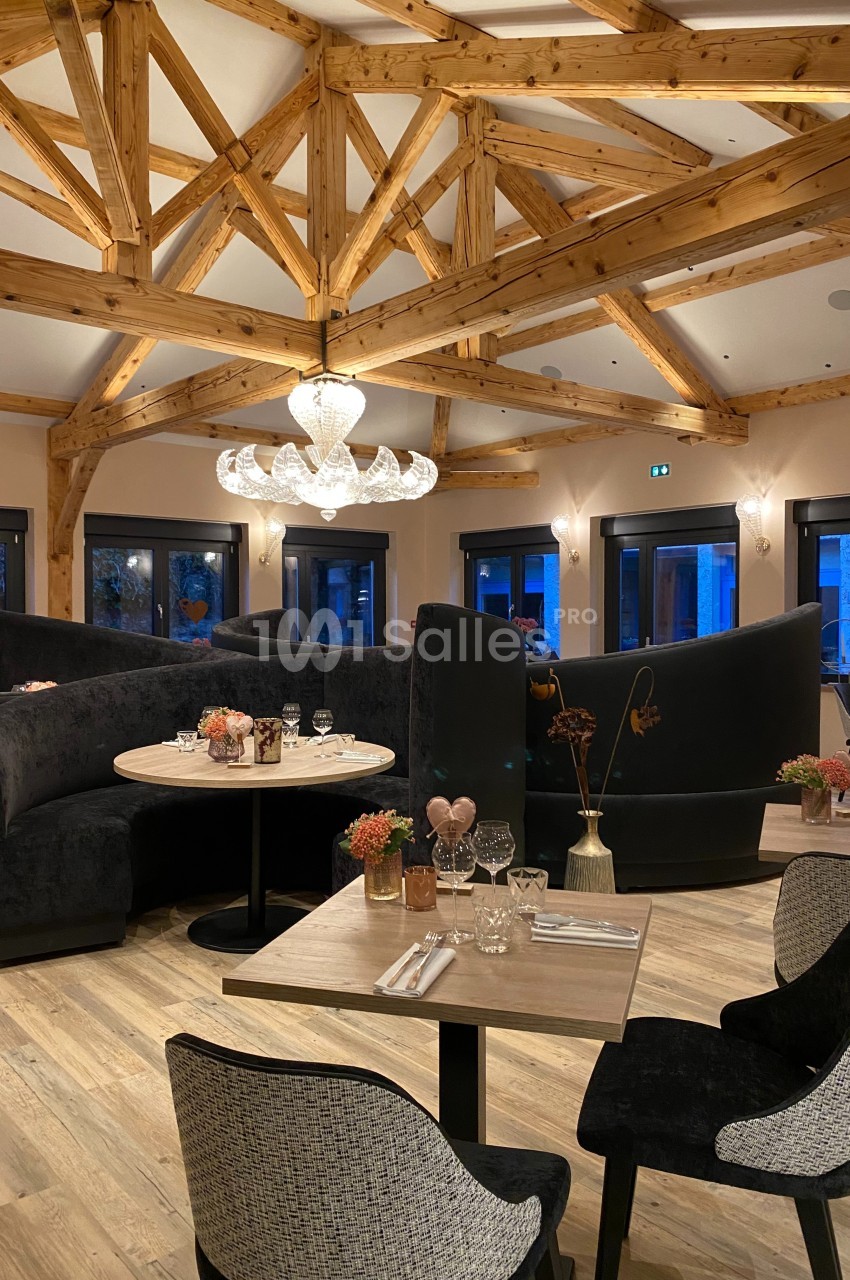 Salle de restaurant élégante avec poutres en bois, tables dressées et banquettes noires dans une ambiance chaleureuse.