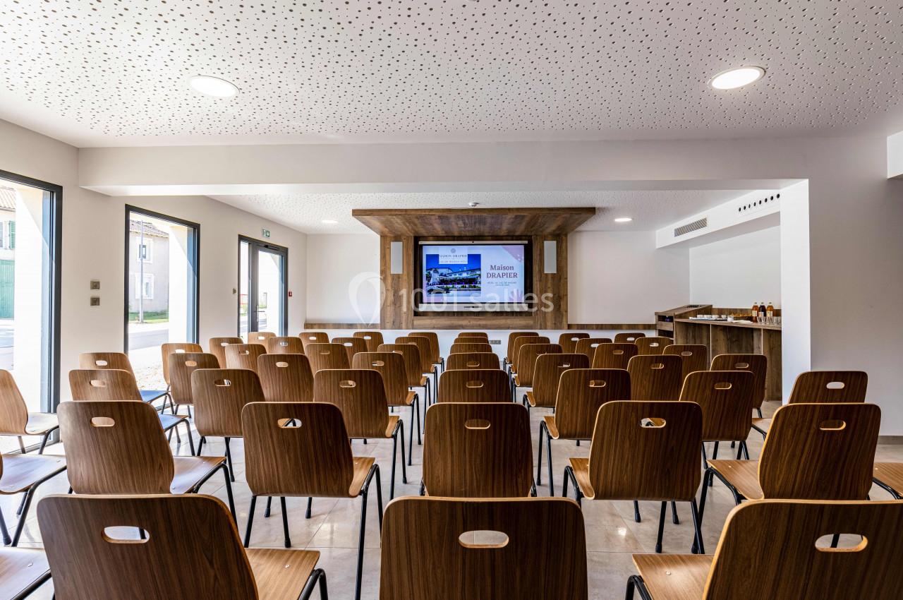 Salle de conférence lumineuse avec des rangées de chaises en bois face à un écran de présentation.