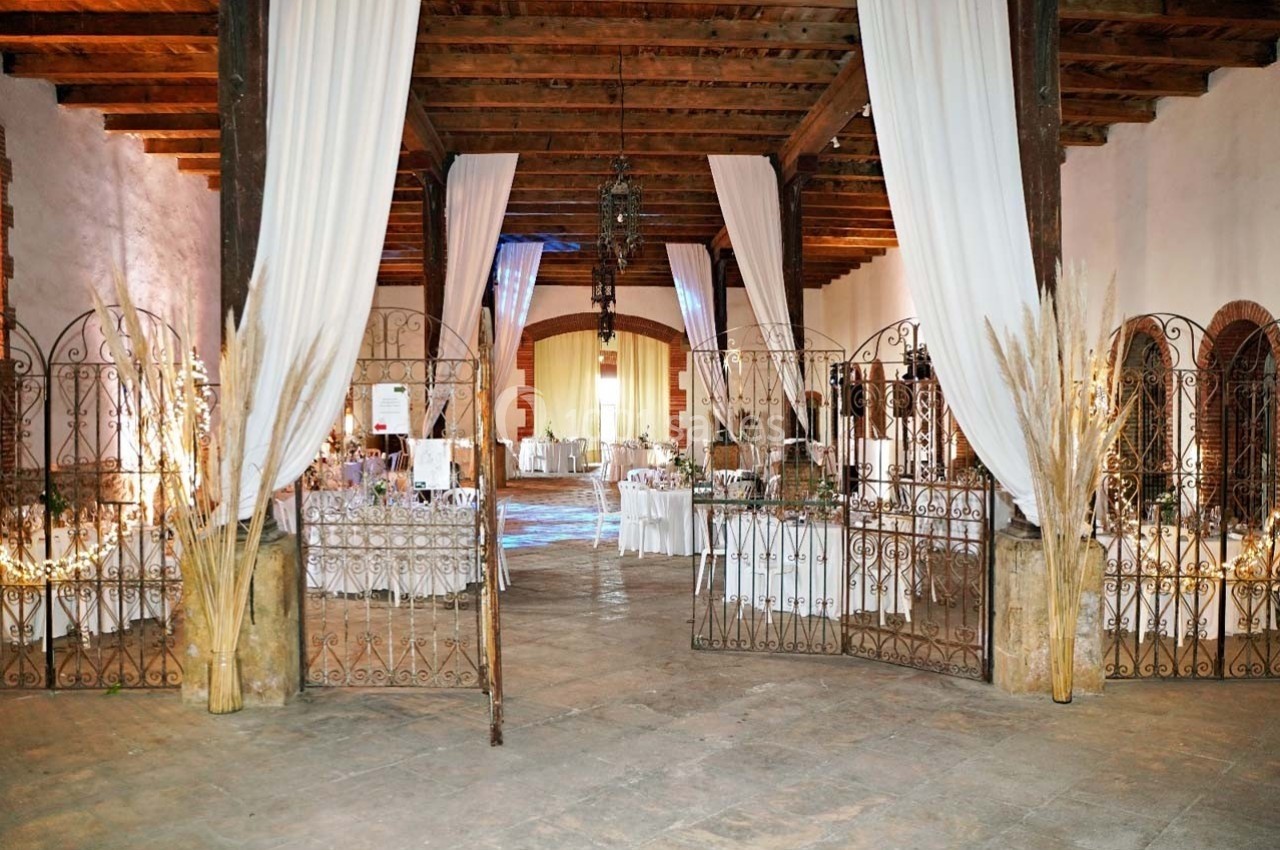 Salle de réception décorée avec des tables dressées, des rideaux blancs suspendus et des guirlandes lumineuses.