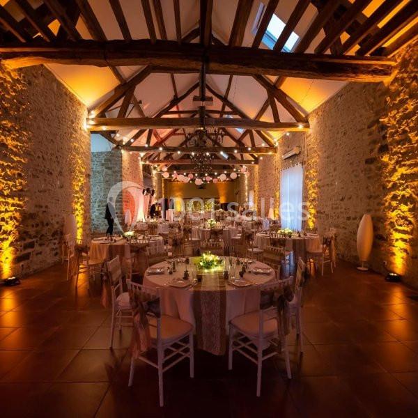 Location salle La Chapelle-Gauthier (Seine-et-Marne) - Nomade-Lodge #4 Salle de réception avec murs en pierre, poutres apparentes, tables décorées et éclairage chaleureux.