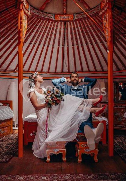 Location salle La Chapelle-Gauthier (Seine-et-Marne) - Nomade-Lodge #6 Un couple en tenue de mariage détendu dans une yourte colorée, la mariée assise et le marié allongé.