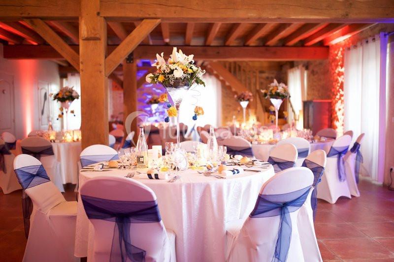 Location salle La Chapelle-Gauthier (Seine-et-Marne) - Nomade-Lodge #7 Salle de réception décorée avec des tables rondes, nappes blanches, chaises ornées de nœuds bleus et centres de table…