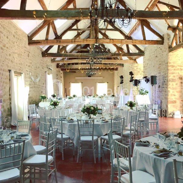 Location salle La Chapelle-Gauthier (Seine-et-Marne) - Nomade-Lodge #8 Salle de réception lumineuse avec des tables rondes décorées, des chaises blanches et une charpente en bois apparente.