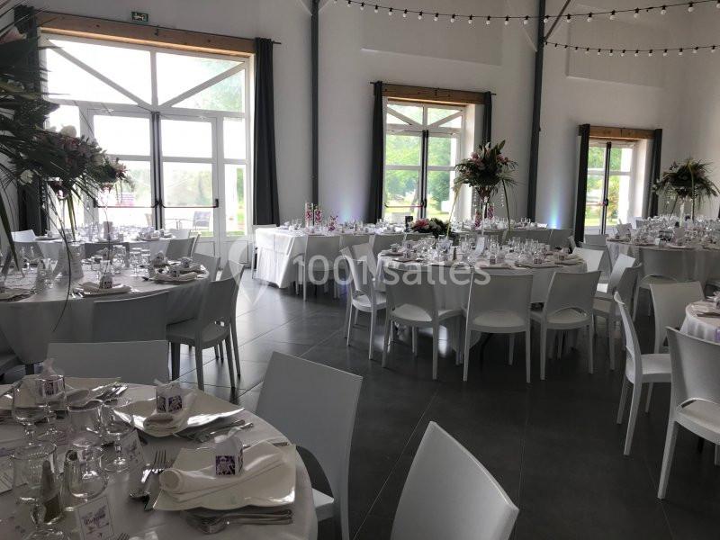 Location salle La Chapelle-Gauthier (Seine-et-Marne) - Nomade-Lodge #11 Salle de réception lumineuse avec tables rondes décorées pour un événement, chaises blanches et grandes fenêtres.