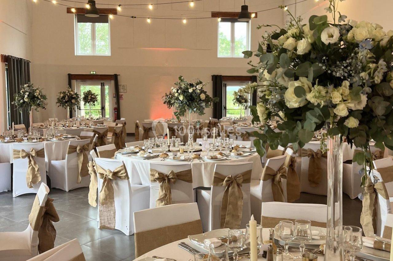 Location salle La Chapelle-Gauthier (Seine-et-Marne) - Nomade-Lodge #32 Salle de réception décorée pour un mariage, avec tables dressées, nappes blanches, chaises ornées et centres de table…