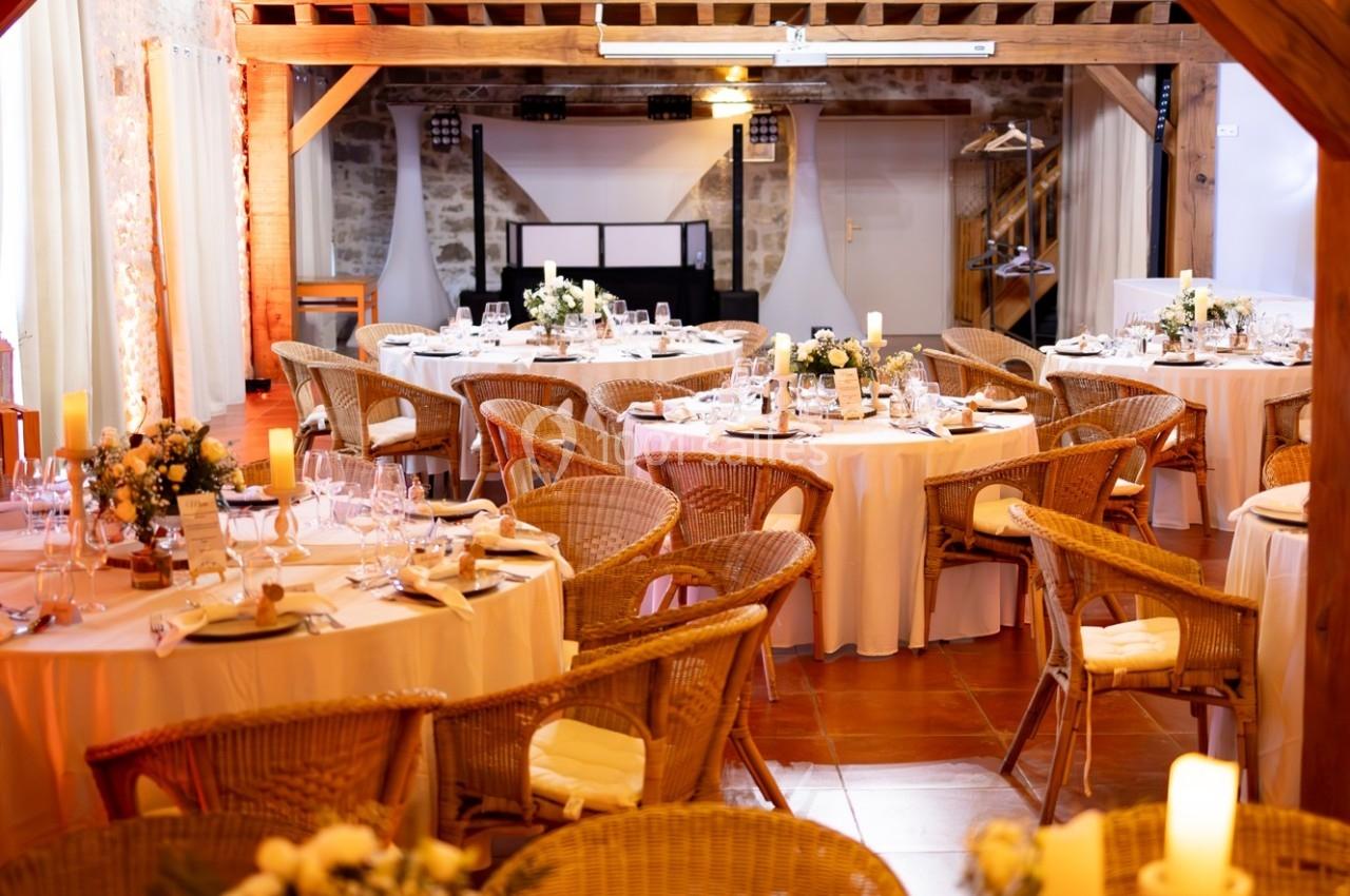 Location salle La Chapelle-Gauthier (Seine-et-Marne) - Nomade-Lodge #27 Salle de réception décorée avec des tables rondes, nappes blanches, chaises en osier et arrangements floraux.