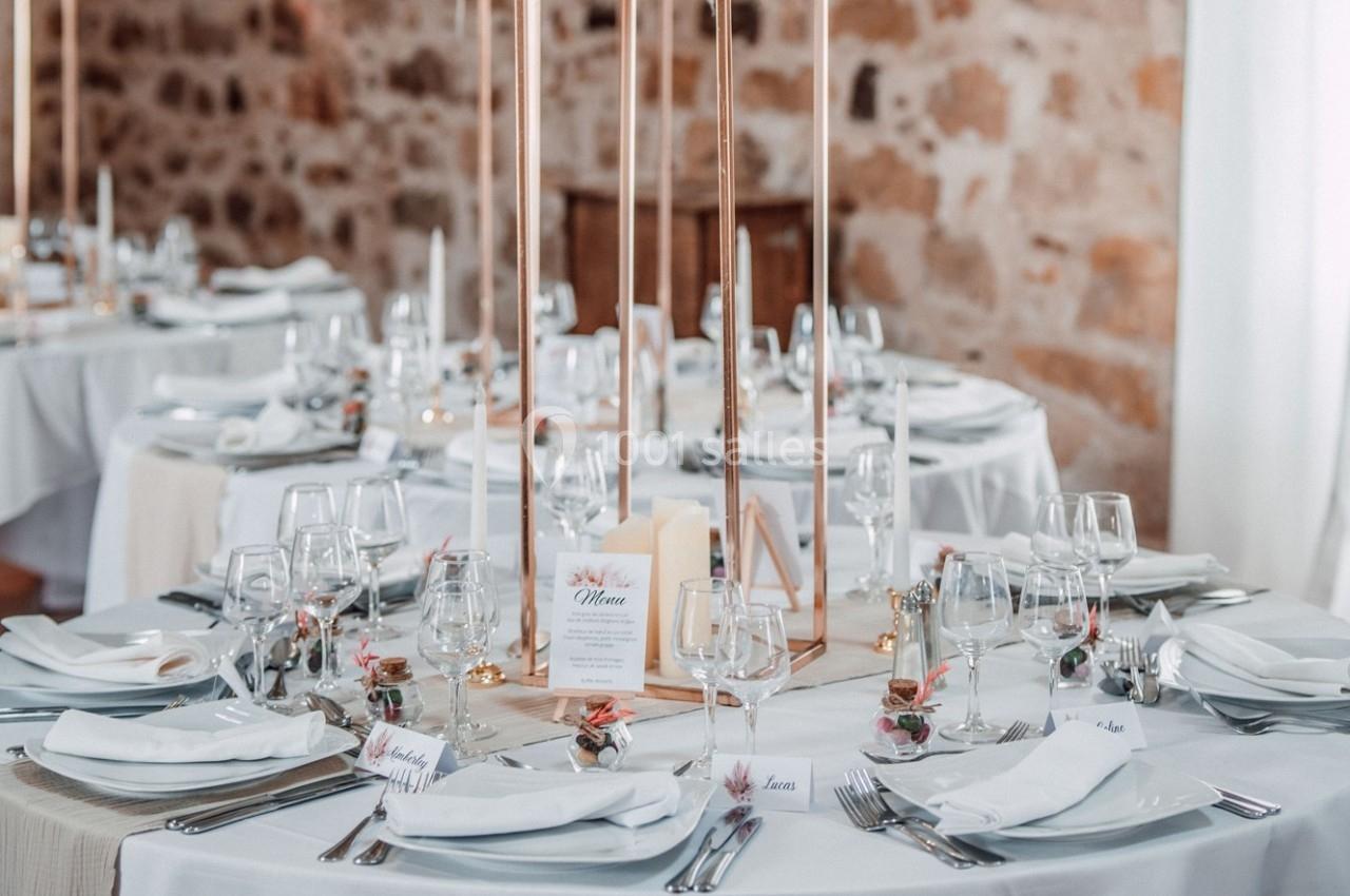 Location salle La Chapelle-Gauthier (Seine-et-Marne) - Nomade-Lodge #35 Tables élégamment dressées pour un événement, avec nappes blanches, bougies et décorations florales dans une salle en pierre.