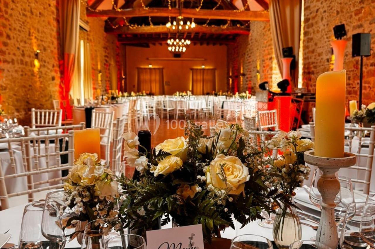 Location salle La Chapelle-Gauthier (Seine-et-Marne) - Nomade-Lodge #41 Salle de réception décorée avec des tables dressées, des chandeliers et des fleurs, dans un cadre en pierre avec poutres…