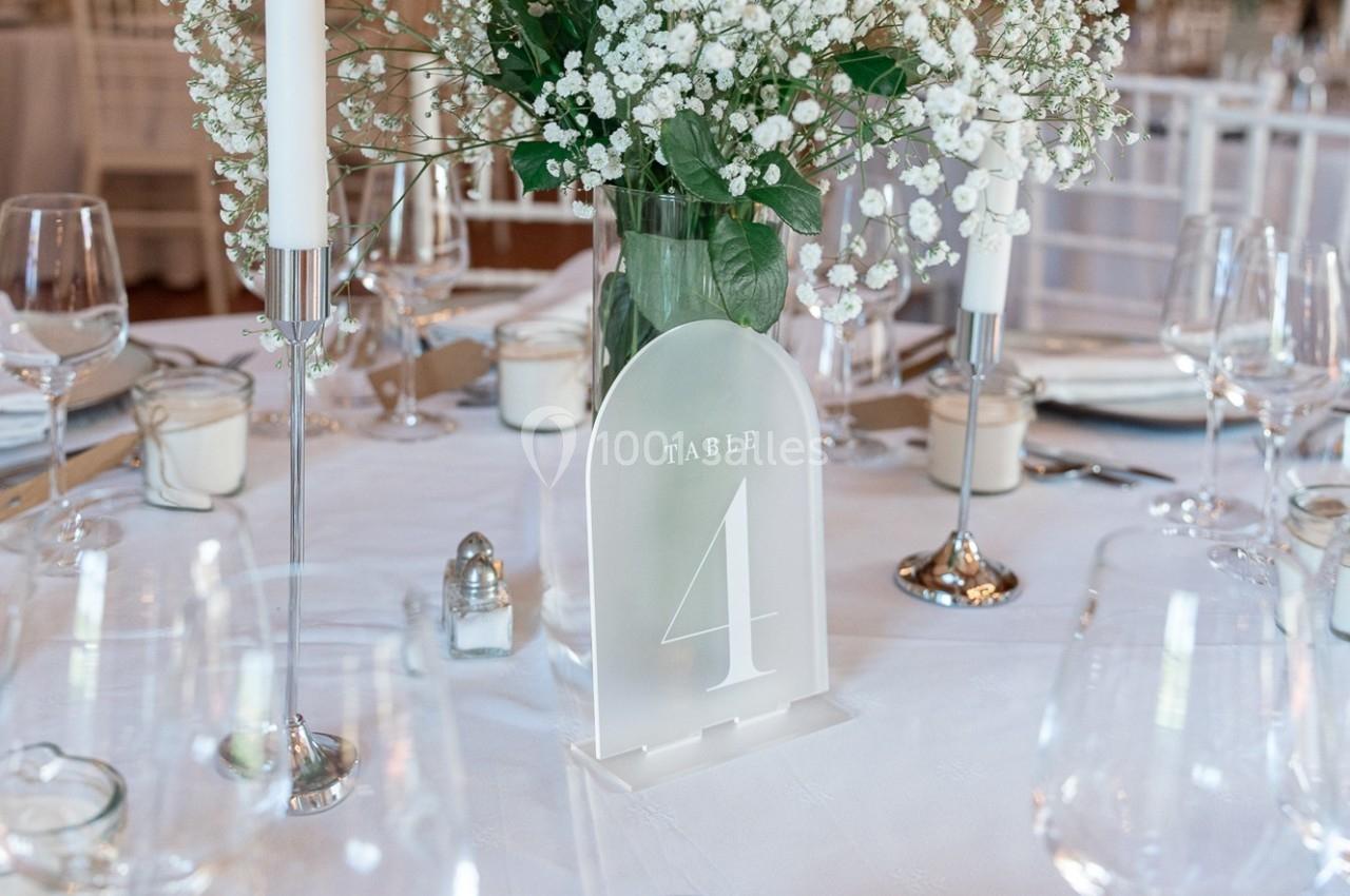 Location salle La Chapelle-Gauthier (Seine-et-Marne) - Nomade-Lodge #44 Centre de table avec fleurs blanches, bougies et panneau indiquant ’Table 4’ sur une nappe blanche élégante.